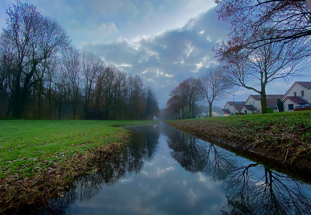 De rand van het bos met daarnaast een woonwijk en in het midden hiervan een sloot.